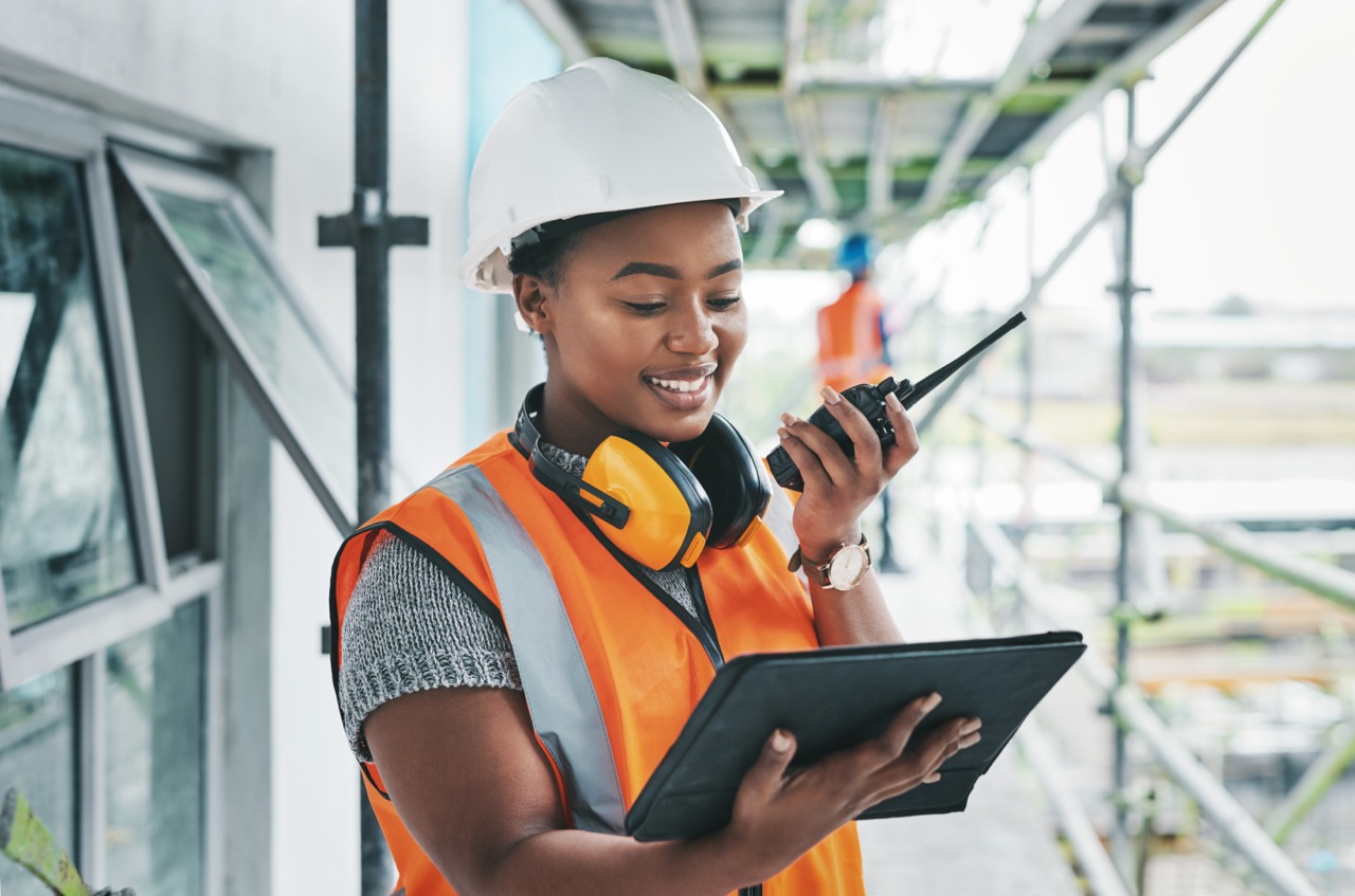 Tablet, engineer and black woman worker planning on a construction site strategy and talking on a walkie talkie. Project management, infrastructure and female contractor doing building assessment.