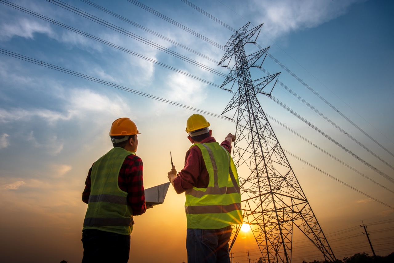 Picture of two electrical engineers checking electrical work using a computer standing at a power station to see the planning work at high voltage electrodes.